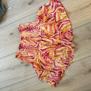 Färgglad kortkjol med volang - Säljer en superfin kortkjol med färgstarkt mönster i rosa, orange, gul och vitt. Kjolen har volang och smockad midja som ger en snygg passform. Perfekt för dig som gillar att sticka ut med din stil! Köpt på västkusten för 500! Står storlek S/M på, men är väldigt töjbar så passar nog XS-L
