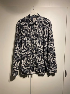 Minimum Svartvit mönstrad skjorta  - Säljer en svartvit skjorta med unikt Minium. Skjortan har klassisk krage, knappar framtill och långa ärmar. Perfekt för dig som vill sticka ut med ett coolt print. Materialet känns mjukt och skönt mot huden. Storlek XL och i fint skick. 