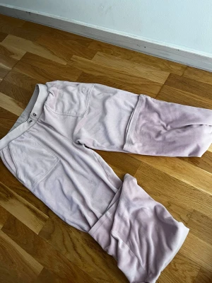 Ljusrosa mjukisbyxor Juicy Couture - Säljer ett par ljusrosa mjukisbyxor från Juicy Couture i mjuk velour. Det är ett litet hål som är ihopsytt men märks inte av, lite smutsiga för de har legat i garderoben länge men med en tvätt blir de som nya igen! Stl 176 men är långa och pösiga på mig som är en Stl s och 173. Snöret har åkt in men går såklart att plocka ur. Pris kan diskuteras men inga skambud