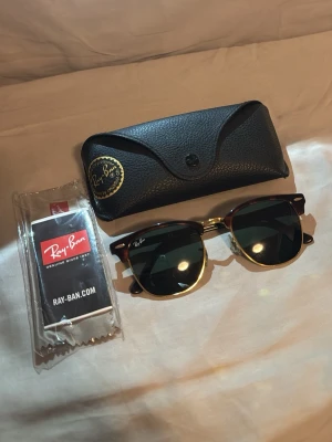 Ray-Ban solglasögon - Snygga Ray-Ban Clubmaster solglasögon med svart och guld båge samt mörka glas. Klassisk retrostil med detaljer i metall och plast. Kommer med originalfodral och putsduk. Perfekta för dig som vill ha en tidlös accessoar till sommaren.