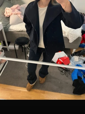Mörkblå kort kappa med bred krage - Snygg mörkblå kappa med bred krage och dubbelknäppning framtill. Modellen är kortare och har en rak passform som ger en modern look. Perfekt för dig som vill ha en stilren och enkel jacka till hösten eller våren. 