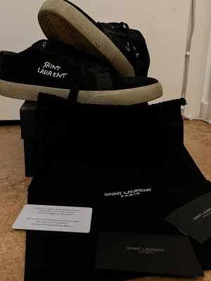 Saint Laurent svarta låga sneakers - Svarta sneakers från Saint Laurent rikigt feta till sommaren som är lite använda men inga stora täcken på användning som sulan lossnat eller stora märken eller slitningar äkta säljer dom för att dom börjar bli försmå. Priser kan diskuteras beror på hur många som är intresserade. Kartong och allt får man med 