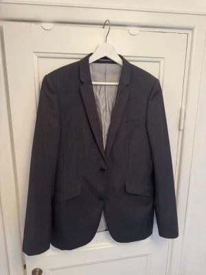 Kavaj Topman grå randig blazer oversize - Säljer en mörkgrå kavaj från Topman London i mycket fint skick. Tyget har en diskret randig struktur som ger ett mer exklusivt intryck.   Klassisk modell med knappstängning framtill och snygg passform.   Storlek: ca S/M (står 36” på lappen och bröstmått 91 cm) Lätt figursydd passform men upplevs lite oversize som S/M  Material: 78% polyester, 22% viskos Foder: 58% polyester, 42% viskos  Endast kemtvätt rekommenderas (kavajen är kemtvättad en gång).  Mycket fint skick  #kavaj #vinted