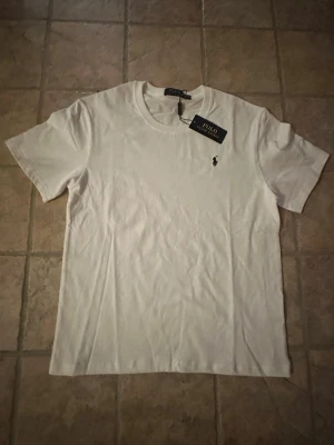 Vit t-shirt från PRL - Klassisk vit t-shirt från PRL  med rund halsringning och den ikoniska lilla broderade loggan på bröstet. Tillverkad i mjuk bomull för en skön känsla. Perfekt basplagg till garderoben.