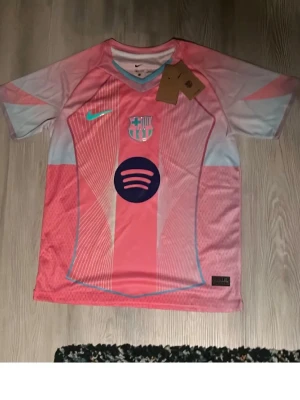 Barça x Nike rosa matchtröja - Säljer en Barcelona matchtröja från Nike i rosa och ljusblått med klubbmärke och Spotify-logga på bröstet. Tröjan har korta ärmar, V-ringning och är tillverkad i lätt polyester som andas. Perfekt för fotboll eller träning.