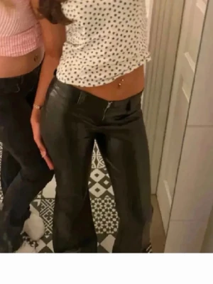 Svarta coated byxor med rak passform - Säljer ett par svarta coated byxor med rak passform och hög midja. Jeansen har en glansig finish som ger en cool look och passar perfekt till både crop tops och oversized skjortor. Materialet är stretchigt för extra komfort och de har klassiska fickor och dragkedja.