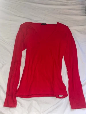 Röd långärmad v-ringad topp - En enkel och snygg röd långärmad topp med v-ringning. Modellen är figurnära och passar perfekt till jeans eller kjol. Tillverkad i mjukt material som känns skönt mot huden. Perfekt för dig som vill ha en basic men ändå stilren topp.