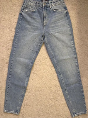 Ljusblå mom jeans från Pieces - Säljer ett par ljusblå mom jeans från Pieces med hög midja och raka ben. Klassisk femficksmodell med dragkedja och knapp framtill. Jeansen har en avslappnad passform och är tillverkade i mjuk denim.