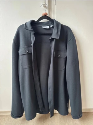 Blå Overshirt S - Stilren blå overshirt från Only & Sons med klassisk krage och två bröstfickor med knappar. Overshirten har raka ärmar och knäppning framtill. Tillverkad i ett mjukt och lite tjockare material som passar perfekt för lager på lager.
