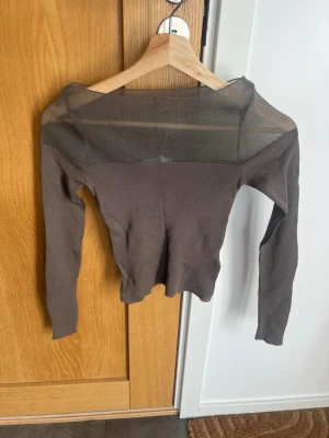 Brun mesh topp från Zara - Säljer en brun långärmad mesh topp från Zara. Toppen har transparent mesh upptill och över axlarna, vilket ger en snygg och trendig look. Perfekt att styla med höga jeans eller kjol för en cool outfit.