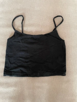 Svart crop top med tunna axelband - Enkel svart crop top med tunna axelband och rak skärning. Perfekt att styla till jeans eller kjol för en clean och stilren look. Tillverkad i mjukt stretchigt tyg som sitter skönt på kroppen.