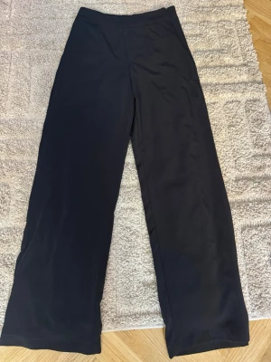 Svarta vida mjukisbyxor - Säljer ett par svarta mjukisbyxor med breda ben och hög midja. Byxorna har en enkel och stilren design utan synliga loggor eller detaljer. Perfekta för chill dagar hemma eller när du vill ha det extra bekvämt. Materialet känns mjukt och stretchigt.