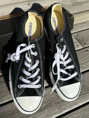 Svarta Converse All Star låga sneakers - Klassiska svarta Converse All Star sneakers med vit tåhätta och vita snören. Skorna har lågt skaft, vit sula och tydliga kontrastsömmar. Tillverkade i canvas med gummidetaljer och metallöljetter. Perfekta för en avslappnad och stilren look. Storlek 41.5 passar 42 också. Skicka prisförslag! Är öppen att diskutera priset