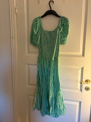 Grön rutig långklänning med puffärm - DEN ÄR INTE I XS UTAN DEN ÄR 170 FÖR BARN! Snygg grön och vit rutig långklänning med puffärmar och öppen rygg. Klänningen har en smockad överdel, volang i nederkant och knyt i ryggen. Perfekt för sommarens alla tillfällen eller till skolavslutning för barn!