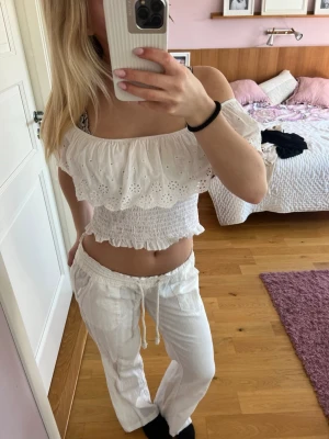 Vit offshoulder croppad topp - Söt vit offshoulder topp med broderade spetsdetaljer och volang. Toppen är croppad och har smockad midja för en bekväm passform. Perfekt till sommaren!