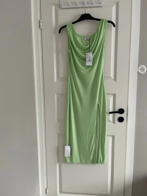 Ljusgrön långklänning med slits - Trendig ljusgrön långklänning med draperad urringning och hög slits på sidan. Klänningen är ärmlös och har en smickrande passform. Perfekt för dig som vill sticka ut med en fräsch färg. Materialet känns mjukt och följsamt.