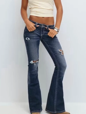 Blå bootcut jeans med slitningar - Från Gina Tricot. Snygga blå bootcut jeans med slitna detaljer och hål på låren och knäna. Jeansen har låg midja, klassiska fem fickor och kontrastsömmar. Perfekta för en avslappnad och trendig look.
