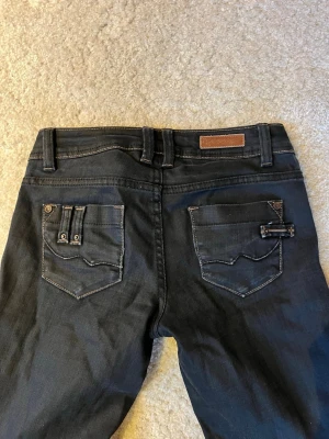 Low waist bootcut jeans  - Snygga svarta jeans. Jeans med kontrastsömmar och unika detaljer på bakfickorna. Klassisk femficksmodell med bälteshällor och knappgylf. Perfekta för dig som vill ha en stilren men ändå personlig look. Pris kan diskuteras 