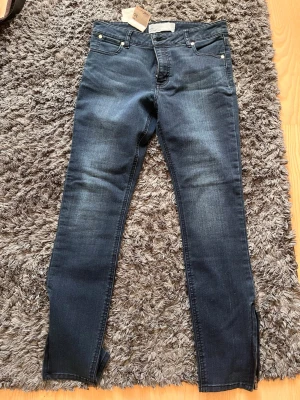 Mörkblå skinny jeans  - Snygga mörkblå skinny jeans med klassisk femficksmodell och diskreta slitningar. Jeansen har dragkedja vid benslut och silverfärgade nitar. Perfekta för en trendig och avslappnad look.