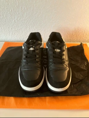 Svarta sneakers från Axel Arigato - Snygga svarta sneakers från Axel Arigato med vita detaljer och vit sula. Skorna har en klassisk låg siluett, svarta skosnören och är tillverkade i läder och mocka. Perfekta för dig som gillar stilrena och moderna sneakers.