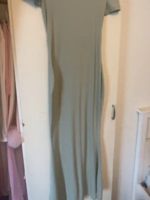 Ljusgrön långklänning med kort ärm - En stilren ljusgrön långklänning med korta ärmar och rak passform. Klänningen har en minimalistisk design utan synliga detaljer och är tillverkad i ett mjukt, stretchigt material som ger en bekväm känsla.