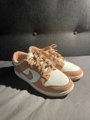 Low vita och rosa sneakers  - sneakers i beige och vitt med klassisk Swoosh på sidan. Ovandelen är i slittåligt läder och har perforerad tå för ventilation. Lågt skaft och matchande beige snören ger en clean och stilren look som passar till det mesta.