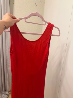 Röd långklänning ärmlös - Snygg röd långklänning med rund halsringning och ärmlös design. Klänningen har en enkel, figurnära passform och är tillverkad i ett mjukt, stretchigt material som känns bekvämt mot huden. Perfekt för dig som vill sticka ut med en klassisk look.