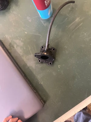 Svart metalladapter med slang - En svart adapter i metall med fyra skruvhål och en fastsatt slang. Passar till olika elektronik- eller maskinprojekt där anslutning av slang behövs. Kompakt och robust design, perfekt för dig som gillar att bygga eller modifiera elektronikprylar.