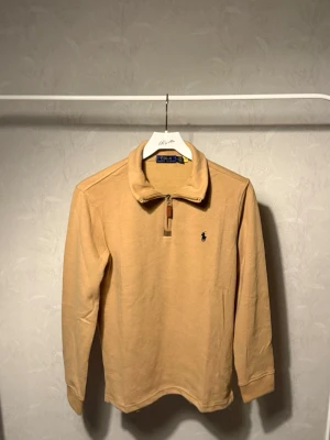 Beige långärmad topp Polo Ralph Lauren - Snygg beige långärmad topp från Polo Ralph Lauren med klassisk krage och half zip-dragkedja. Broderad logga på bröstet och mjukt bomullsmaterial. Perfekt för en clean och stilren look.