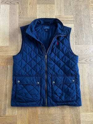Ralph lauren väst - Quiltad ralph lauren väst i fint skick förutom att den har ett litet brännmärke vid loggan. Det går nog att laga ganska enkelt.
