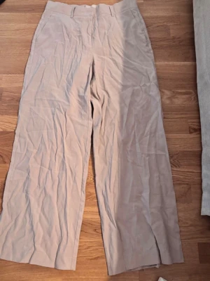 Beige linnebyxor Pernilla Wahlgren - Snygga beige linnebyxor från Pernilla Wahlgren med raka, vida ben och hög midja. Byxorna har bälteshällor och är tillverkade i ett lätt och luftigt linnematerial, perfekta för en avslappnad och trendig look.