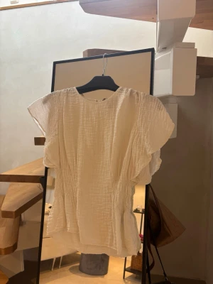 Vit blus med korta arm  - Säljer en luftig vit blus i mjukt, krinklat tyg. Blusen har rund halsringning, korta ärmar och fina rynkdetaljer. 