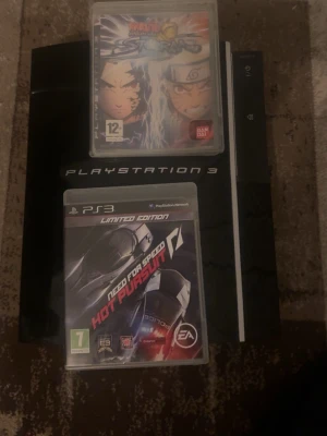 PlayStation 3 med två spel - Säljer en svart PlayStation 3 med klassisk design från Sony. Konsolen är i plast och har en blank finish. Medföljer två spel: Naruto Ultimate Ninja Storm och Need for Speed Hot Pursuit. Perfekt för dig som gillar både fighting och racing! Det finns Samt GTA 