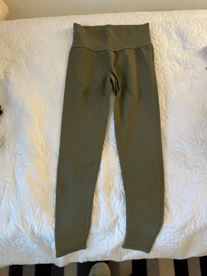 Olivgröna leggings med hög midja - Snygga olivgröna leggings med hög midja och ribbade detaljer längst ner på benen. Stretchigt material som sitter tight och formar sig efter kroppen. Perfekta för en trendig och bekväm look.