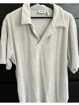 Ljusgrå frottétopp från Weekday - Säljer en ljusgrå topp från Weekday i mjuk frotté. Toppen har korta ärmar, öppen krage och relaxed fit. Perfekt för dig som gillar en chill och modern stil.