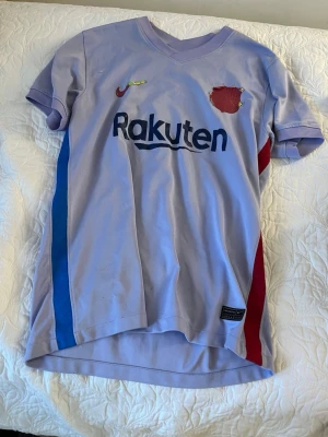 Ljuslila FC Barcelona matchtröja - Snygg ljuslila FC Barcelona matchtröja från Nike med Rakuten-tryck på bröstet och Unicef-logga på ryggen. Tröjan har blå och röda detaljer på sidorna samt klubbmärke på bröstet som tyvärr har åkt av Perfekt för dig som älskar fotboll och vill representera Barca.