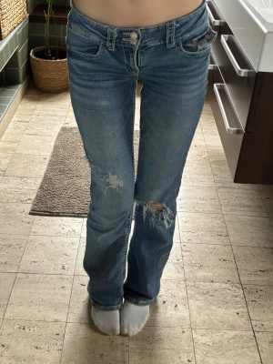 Blå slitna jeans från Gina Tricot - Ett par supersnygga blå jeans från Gina Tricot! Är lowrise, bootcut och har slitningar på båda benen. Säljer pågrund av att de känns inte som att de passar mig ❤️Passar mig perfekt som är 173 cm.  Kostade ca 450, men kan gå ner.