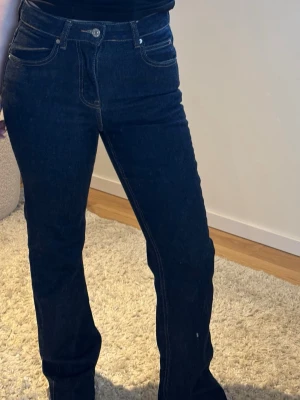 Gina jeans  - Säljer ett par mörkblå jeans med raka ben och hög midja. Klassisk femficksmodell med kontrastsömmar och knappgylf. Jeansen har en tidlös look och passar perfekt till en avslappnad stil. 🌸🌟😍🩷🎉 Perfekt för alla tillfällen! 🌟