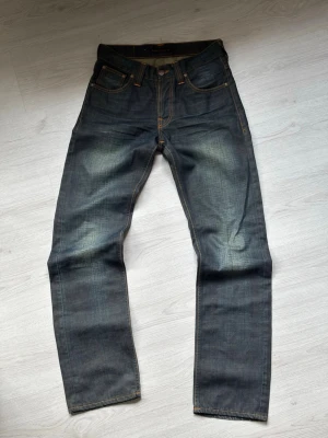 Nudie jeans - Ett par lite mer vintage nudies, modell straight sven. Står w29 L34 fast sitter som w28/27 L32. På den sista bilden syns vart knappen hade bilivit reparerad, reparationen utfördes hos nudie. Jag på bilden är 179cm 62kg. Skriv vid funderingar✌️