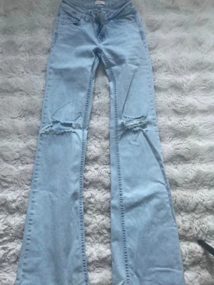 Ljusblå bootcut jeans från nelly  - Säljer ett par ljusblå bootcut jeans med detaljer över knäna och broderade fickor bak. Jeansen har låg midja. Demr lite lite slitna vid fötterna där bak 