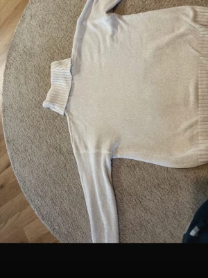 Ljusbeige polotröja stickad - Mysig ljusbeige stickad polotröja med ribbad krage och muddar. Tröjan har lång ärm och är tillverkad i ett mjukt material som passar perfekt för kyligare dagar. Enkel och stilren design som är lätt att matcha.