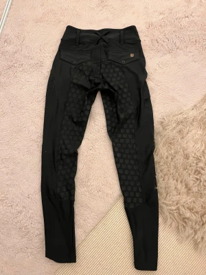 MD ridbyxor  - Säljer ett par svarta ridleggings från maya delorez med helskoning i silikon för extra grepp. De har fickor med lock bak, bälteshällor och en diskret logga på låret. Materialet är stretchigt och följsamt, perfekt för ridning.