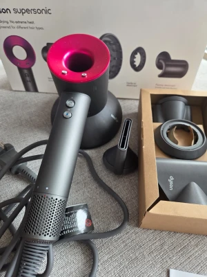 Dyson Supersonic hårfön grå/rosa - Dyson Supersonic hårfön i snygg grå och rosa design. Kommer med flera munstycken för olika stylingmöjligheter. Tillverkad i plast och metall, ergonomisk form och modern look. Perfekt för dig som vill ha snabb och skonsam hårtorkning. Använda några gånger