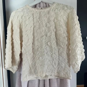 Krämvit blus med trekvartsärm  - Supersöt beige blus med strukturmönster. Blusen har rund halsringning och trekvartsärm. Passar till både skola/jobb eller till fest. Nypris är 499 kr
