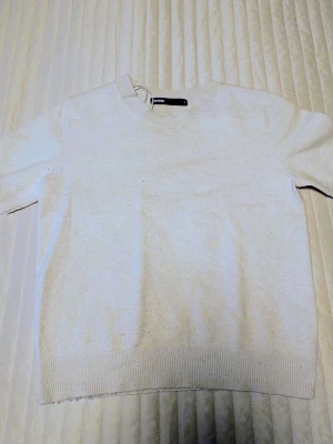 Vit stickad tröja från Bik Bok - Snygg vit stickad tröja från Bik Bok med rund halsringning och korta ärmar. Tröjan har ribbade muddar vid ärmslut och nederkant, vilket ger en clean och stilren look. Perfekt att matcha med jeans eller kjol för en enkel outfit.