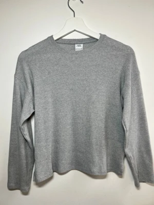 Grå stickad tröja från Zara - En enkel och stilren grå stickad tröja från Zara med rund halsringning och långa ärmar. Tröjan har en rak passform och är tillverkad i mjukt material som passar perfekt till alla typer av outfits.