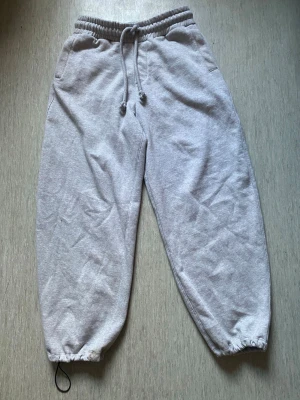 Grå mjukisbyxor från Bershka - Säljer ett par grå mjukisbyxor från Bershka med resår i midjan och dragsko. Byxorna har två sidofickor och resår vid bensluten. Perfekta för chill dagar och riktigt sköna tack vare det mjuka materialet.