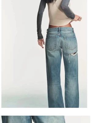 Blå baggy jeans med slitningar - Säljer ett par ljusblå baggy jeans med slitningar på både fram- och baksida. Jeansen har raka ben, klassisk femficksmodell och låg midja. Perfekta för en avslappnad och trendig look.