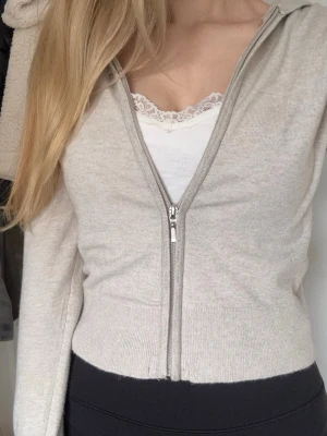 Gina Zip hoodie - Säljer en beige hoodie med dragkedja framtill och huva. Modellen är croppad med långa ärmar och ribbade muddar. Materialet känns mjukt och stretchigt. Passar till det mesta och är enkel att styla. Strorlek 170 men sitter som XS/S.