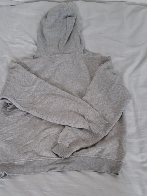 Grå UCLA hoodie med tryck - Säljer en grå hoodie från UCLA med stort gult och vitt tryck på bröstet. Klassisk modell med huva och dragsko, samt ribbade muddar vid ärmar och nederkant. 